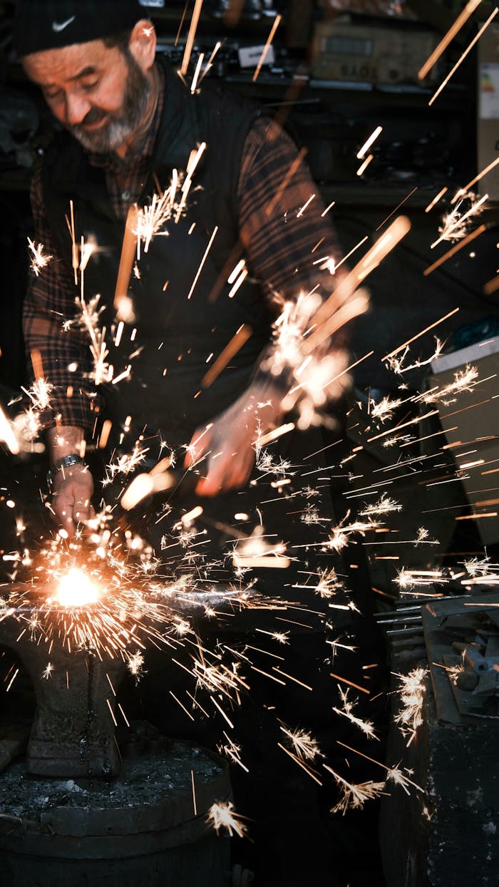 Adult working with metal, creating bright sparks in an industrial workshop setting.